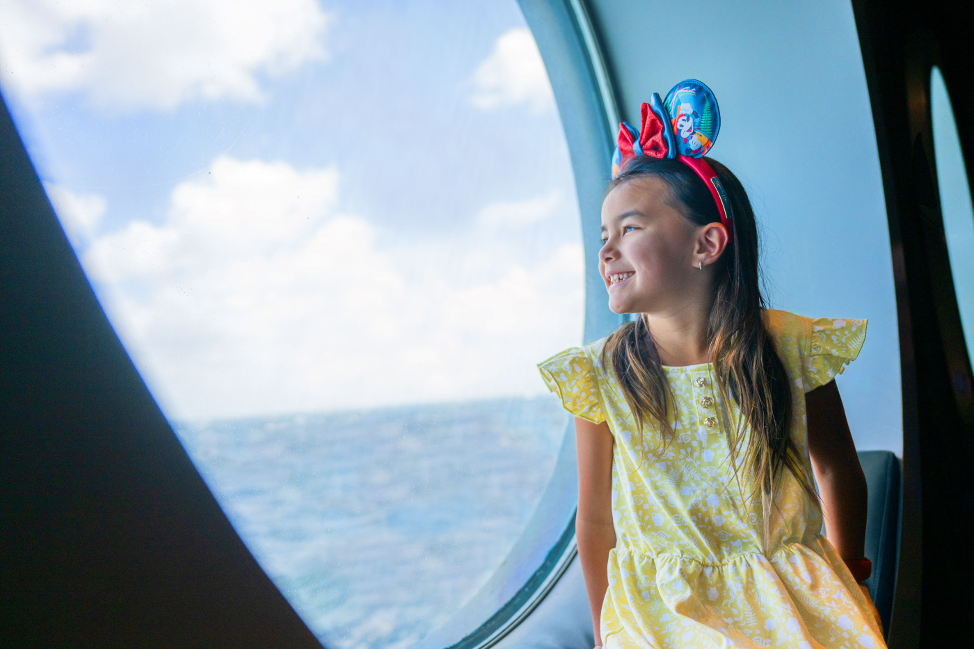 Girl with Mickey ears looking out porthole