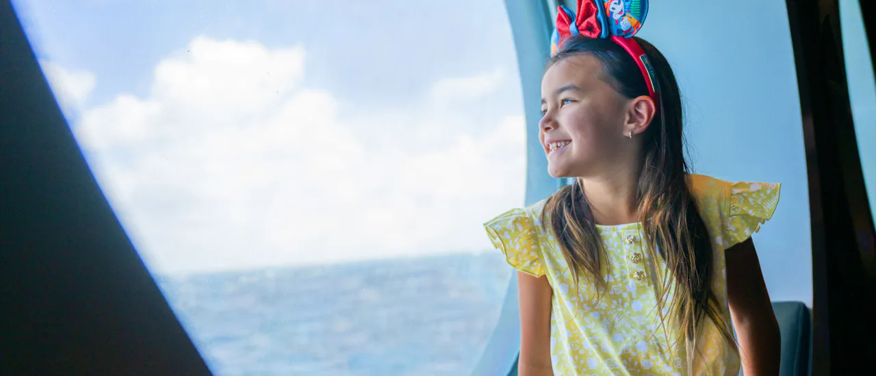 Girl with Mickey ears looking out porthole