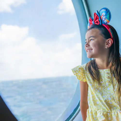 Girl with Mickey ears looking out porthole
